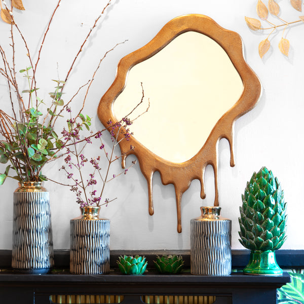 A mirror on the wall with a green artichoke ornament and multiple vases on a table