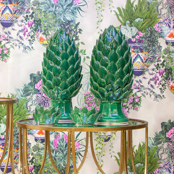 Two green artichoke ornaments on a gold table against floral wallpaper