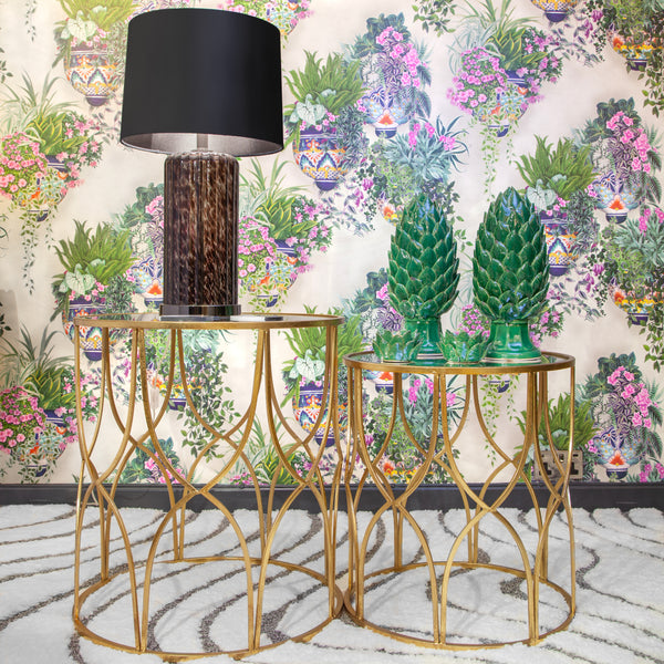 Two round gold side tables, one with a lamp and the other with two green artichoke ornaments