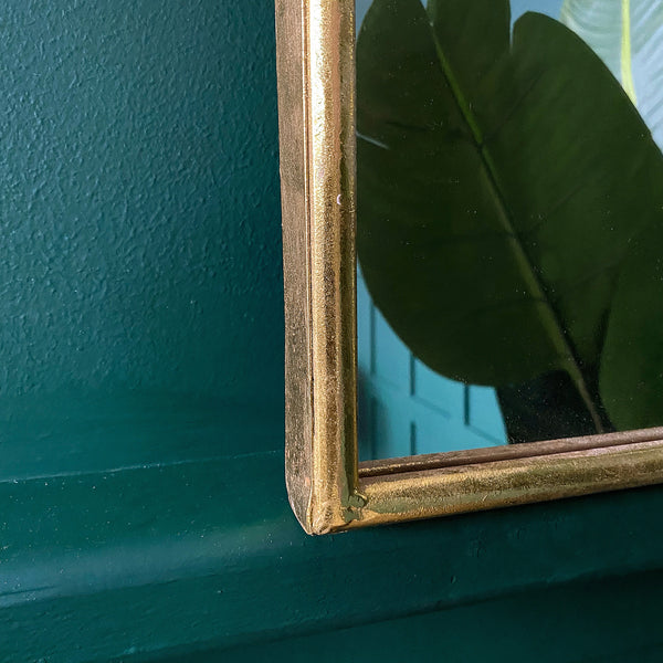 Close-up of a gold framed mirror hanging on a green wall