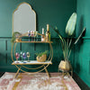 A gold Moroccan mirror on the wall with a bar cart and plant pots placed in front of it