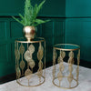 Two gold side tables with intricate cutout designs, one holding a potted fern