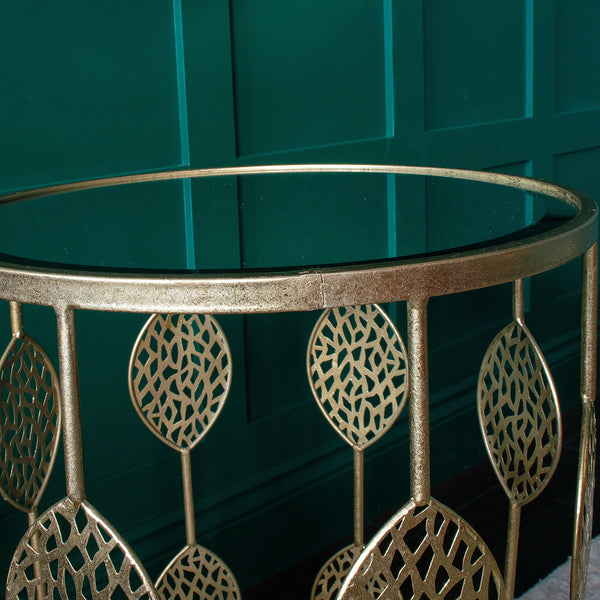 Close-up of a gold side table with intricate leaf design and glass top