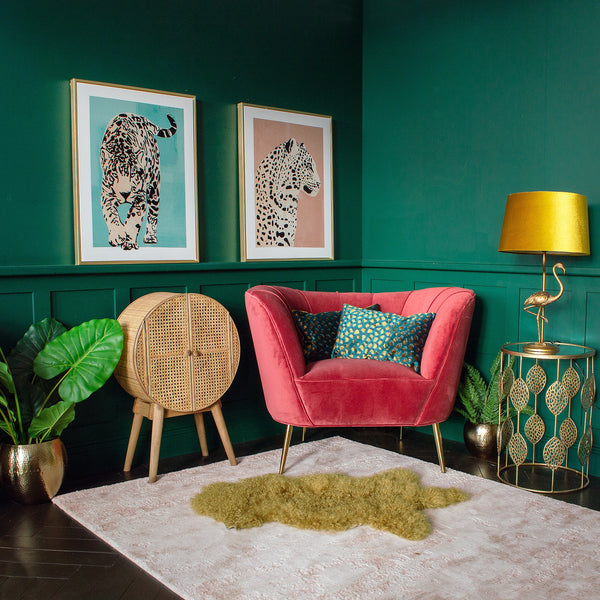 A green room corner with a red armchair, a gold side table, and two framed wall prints