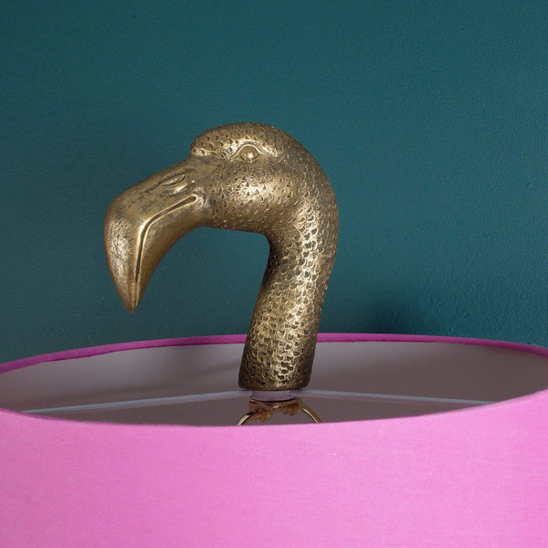 A pink lamp shade with a gold flamingo bird perched on top