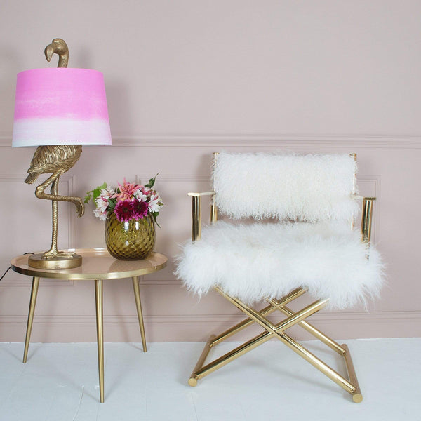 A gold flamingo lamp and a vase on a side table beside a gold fur chair