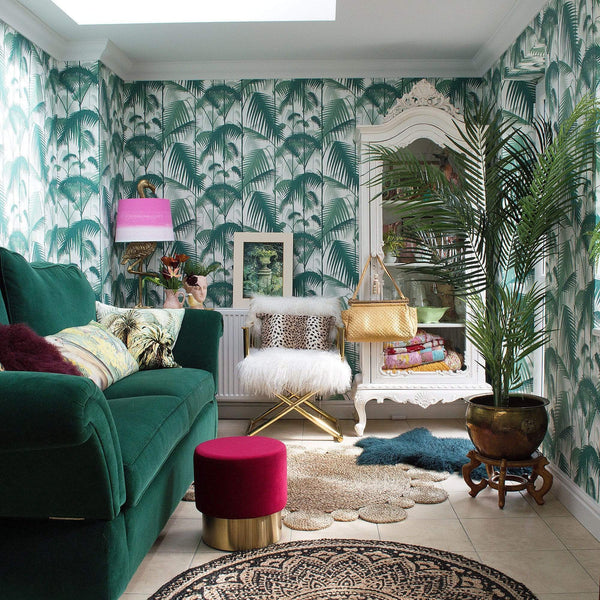 A room with a green sofa, cushions, rugs, a chair, a flamingo lamp, and plants