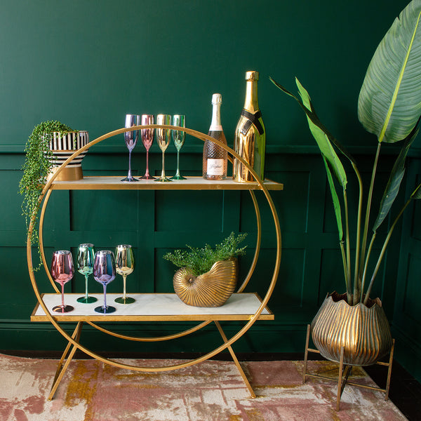 A round drinks trolley with various decorative items including a gold shell planter