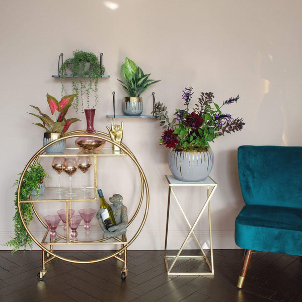 A gold round drinks trolley stocked with plants and glassware