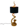 A sleek gold snake table lamp with a black shade on a white background