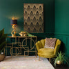 A room with gold wall art, a console table, a velvet armchair, a gold snake table lamp, and plants
