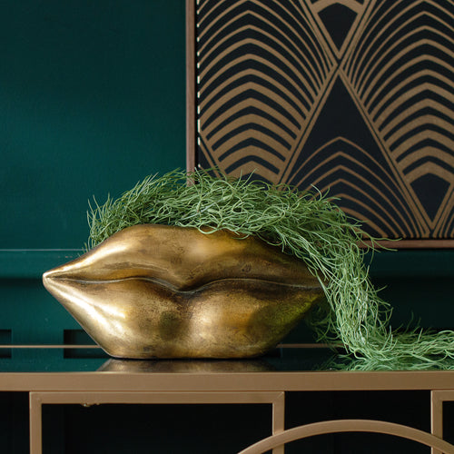 A golden lips planter on a table with a green plant