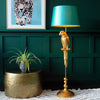 A golden parrot floor lamp with a turquoise shade next to a plant pot and a framed leopard print