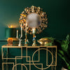 A console table with various bird candle holders, a hare lamp, a planter, and a round wall mirror behind it