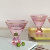 Two pink martini glasses with gold rims, one on a marble slab with olive skewers, and the other on a gold tray