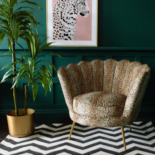 A leopard print chair next to a plant pot on a rug, with a framed picture of a leopard on the wall