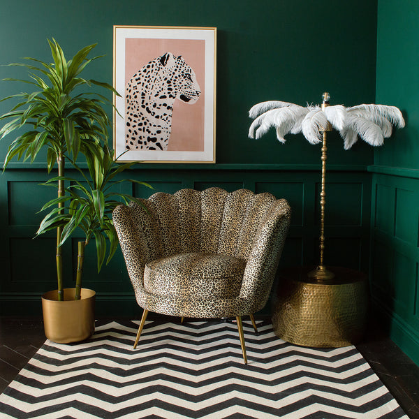 A leopard print chair next to a plant pot, a floor lamp, a rug, and a framed leopard wall art
