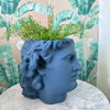 Side view of a blue head-shaped planter with green foliage placed on a round marble table