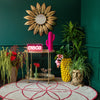 A room featuring a wall mirror, a bar cart with various decorative items, a rug, multiple plant pots, and vases